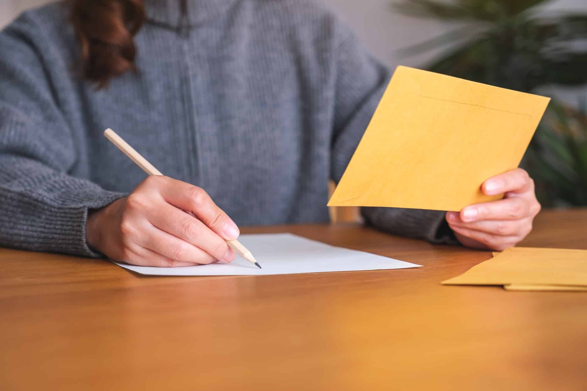 Closeup image of a young woman writing on a letter and envelopes