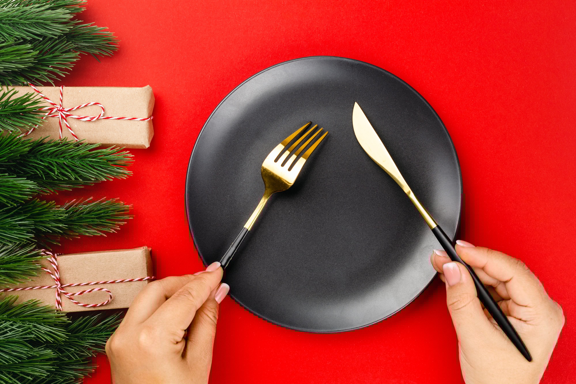 gold cutlery with black handles crossed over black plate on red table the concept of New Year dinner
