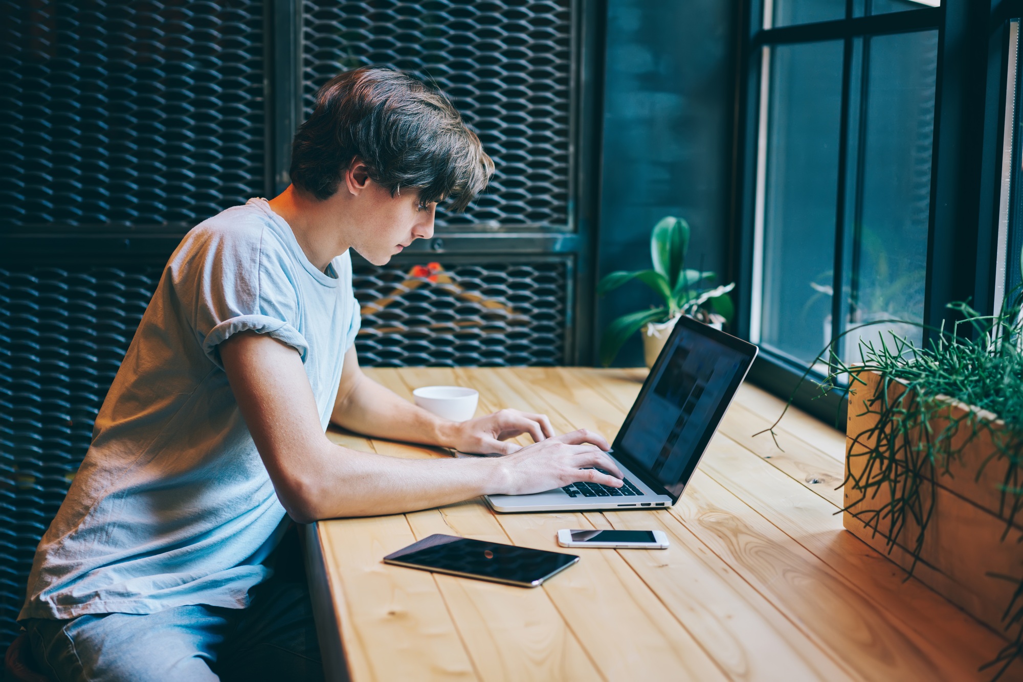 Serious man browsing laptop located on wooden table with gadgets